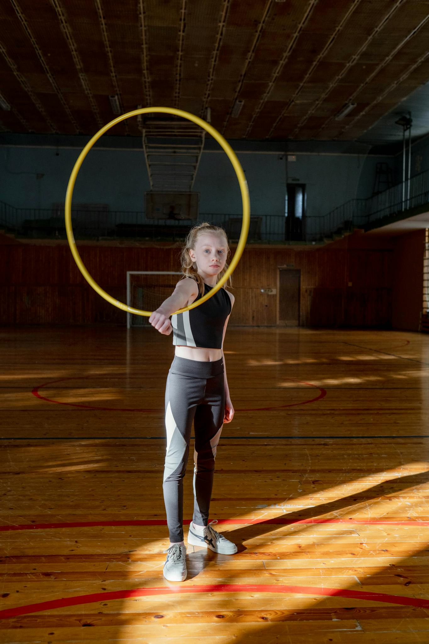 A child in sportswear practicing hula hooping indoors, full of sunlight and movement.