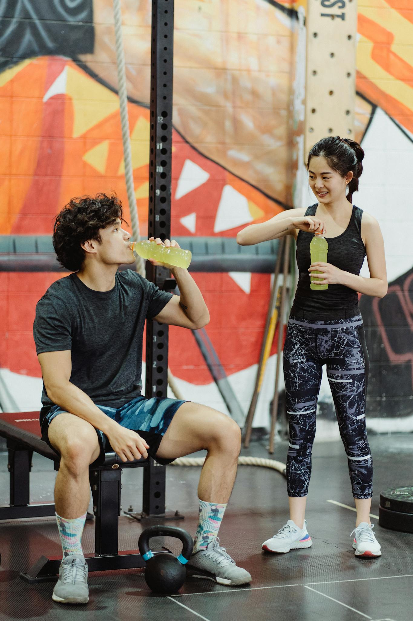 Asian couple in activewear hydrating with drinks in a gym setting. Vibrant and energetic.